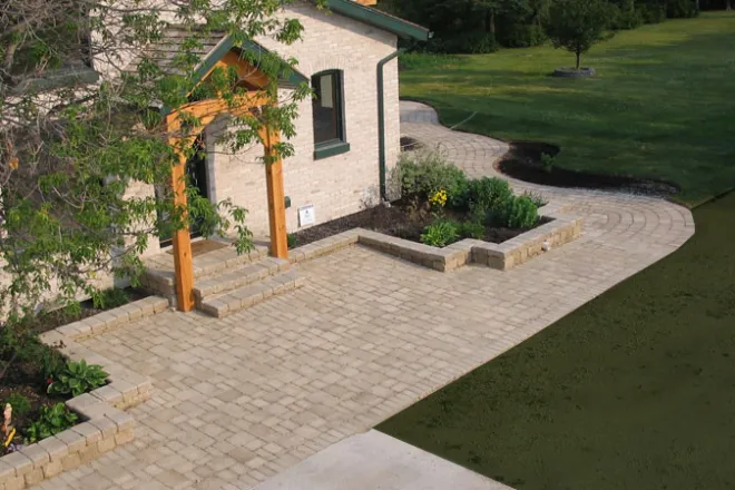 Elegant residential driveway constructed with interlocking stone pavers, bordered by lush landscaping and leading to a modern garage and stairway entrance.