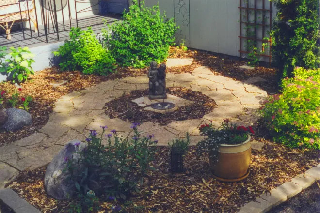 Interlocking stone driveway under construction in front of a modern wood-paneled home, with paving stones being carefully installed on a gravel base.