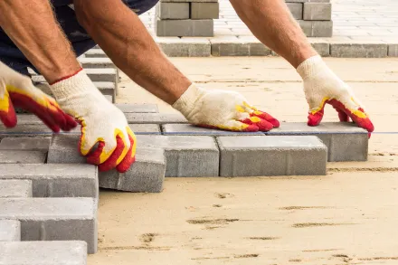 Close-up of a worker installing interlocking paving stones on a sand base, carefully aligning the bricks by hand for a professional driveway finish.